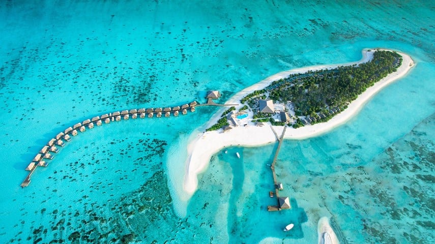 Pamje ajrore e një ishulli tropikal me ujëra turkeze dhe vila mbi ujë, që ilustron pushimet në Zanzibar dhe Maldive.