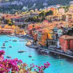 Pamje panoramike e Côte d’Azur me bregdetin mesdhetar, ndërtesa shumëngjyrëshe dhe detin e kaltër në Rivierën Franceze.